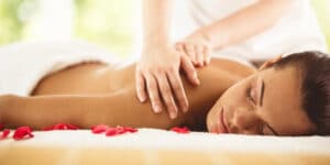 A person receiving a back massage with rose petals scattered on the bed